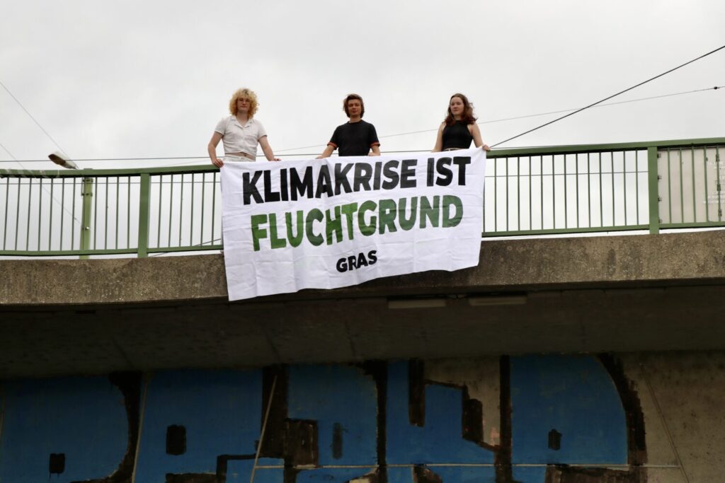 Drei Demonstrierende mit einem Banner mit der Aufschrift Klimakrise ist Fluchtgrund auf einer Brücke